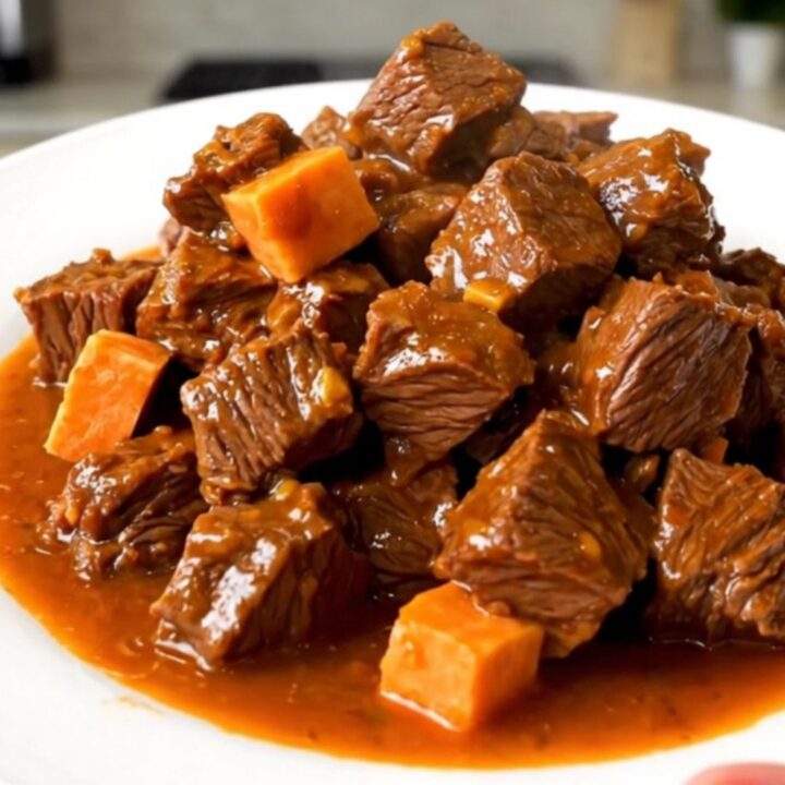 A top-down view of a black oval slow cooker filled with chunks of beef, diced sweet potatoes, and broth.