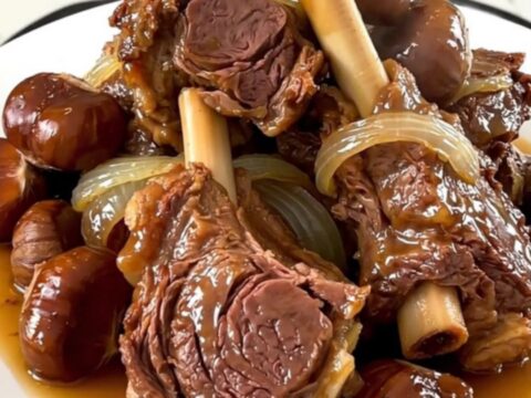 A close-up of tender lamb shoulder with glazed chestnuts and onions in a slow cooker.