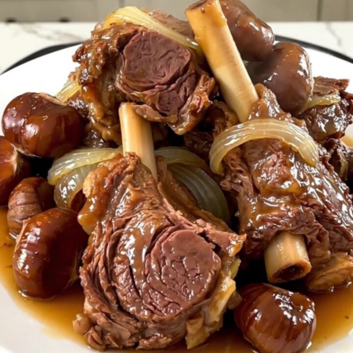 A close-up of tender lamb shoulder with glazed chestnuts and onions in a slow cooker.