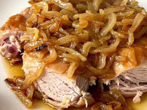 A close-up view of slow cooker turkey yassa served on a white plate with tender onions and a savory sauce.