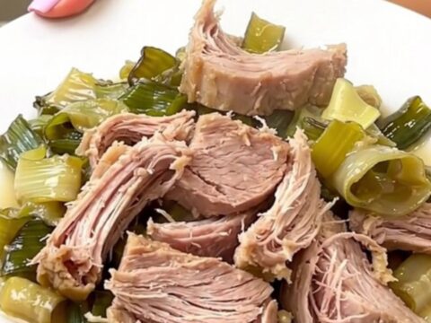 A rustic slow cooker pork roast served on a white plate with creamy leeks and cider sauce.