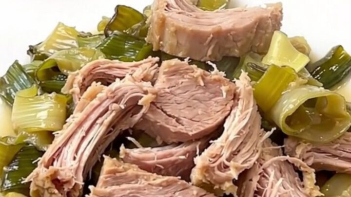 A rustic slow cooker pork roast served on a white plate with creamy leeks and cider sauce.