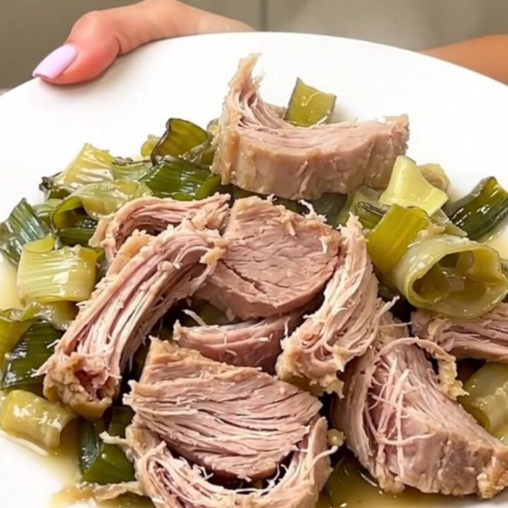A rustic slow cooker pork roast served on a white plate with creamy leeks and cider sauce.