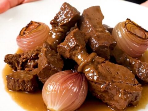 Tendrons de veau braisés et échalotes confites dans une assiette blanche avec une vapeur légère.