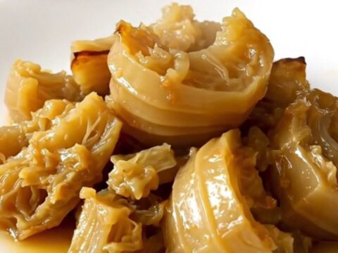 A close-up of tender, braised celeriac cubes served on a white plate with fresh thyme.