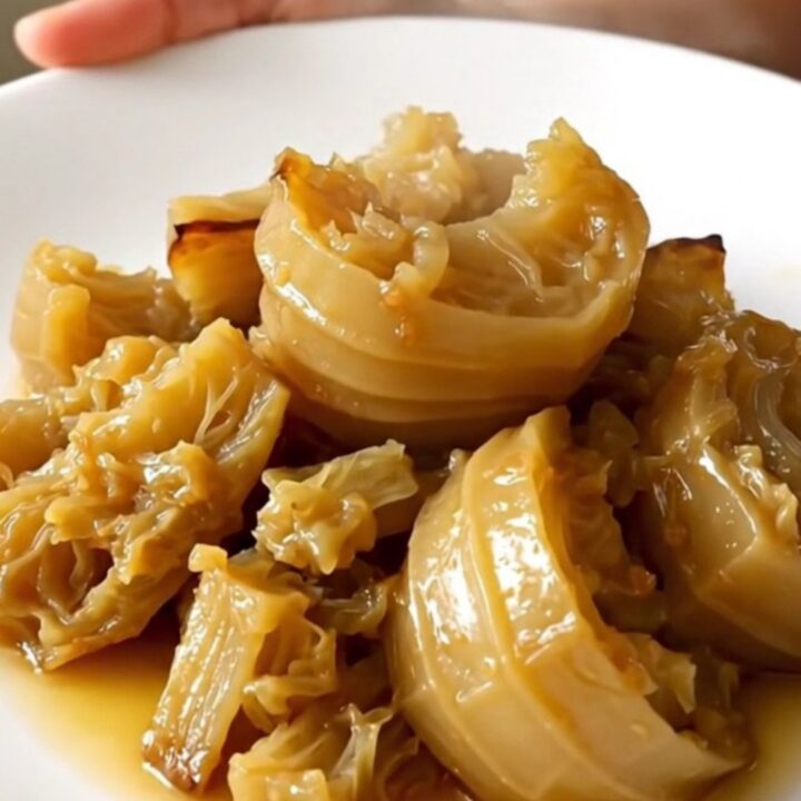 A close-up of tender, braised celeriac cubes served on a white plate with fresh thyme.