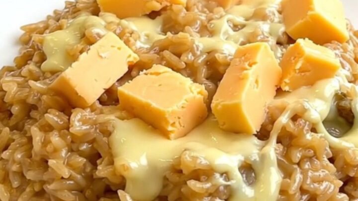 A top-down view into a black slow cooker showing raw rice, sliced onions, and chunks of Maroilles cheese.