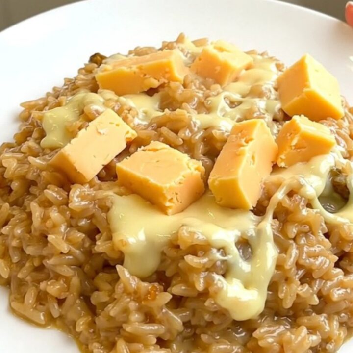 A top-down view into a black slow cooker showing raw rice, sliced onions, and chunks of Maroilles cheese.