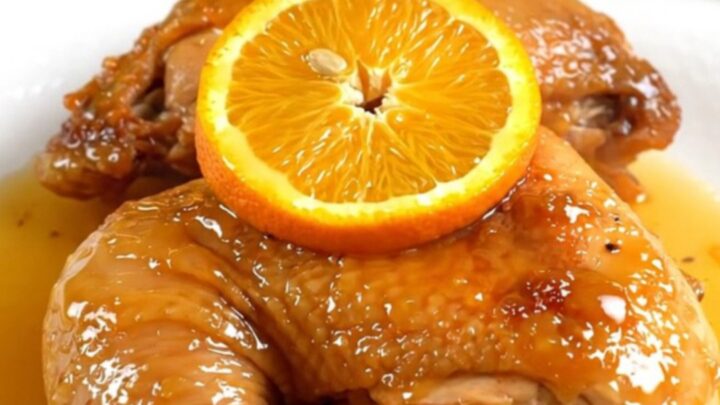 A close-up of tender orange rosemary chicken in a slow cooker with fresh citrus slices.