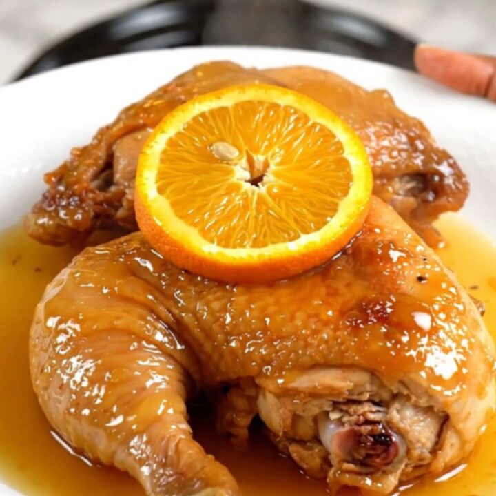 A close-up of tender orange rosemary chicken in a slow cooker with fresh citrus slices.
