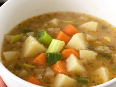 A rustic bowl of steaming vegetable soup featuring chunks of leek, carrot, potato, and turnip.