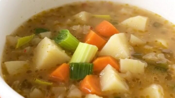 A rustic bowl of steaming vegetable soup featuring chunks of leek, carrot, potato, and turnip.