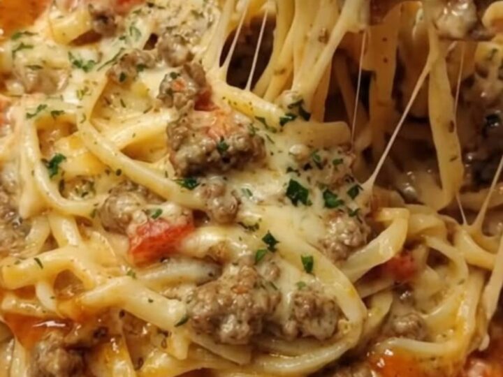 A close-up of a fork lifting cheesy linguine coated in a glossy, rich parmesan sauce with a dramatic cheese pull.