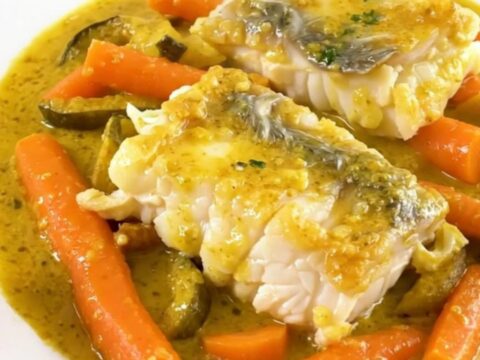 A top-down view of raw haddock fillets, sliced carrots, and onions in a slow cooker.