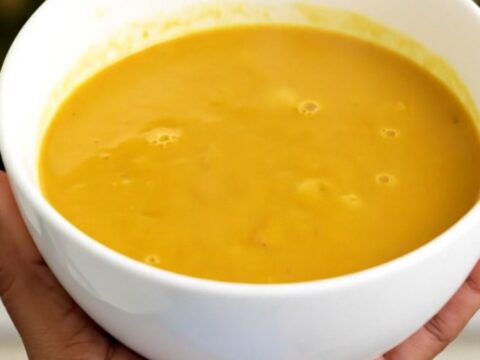 A steaming bowl of vibrant, golden turmeric and coconut pumpkin soup on a white surface.