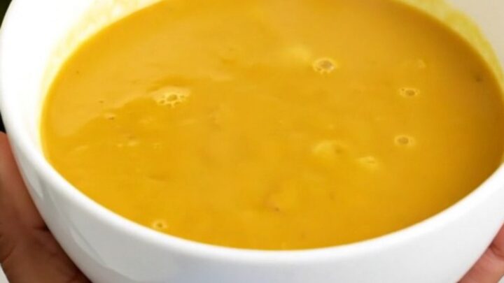 A steaming bowl of vibrant, golden turmeric and coconut pumpkin soup on a white surface.