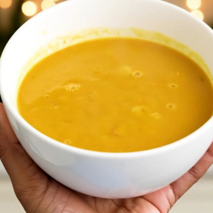 A steaming bowl of vibrant, golden turmeric and coconut pumpkin soup on a white surface.