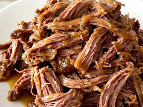 Gigot d'agneau fondant servi sur une assiette blanche avec une sauce brillante.