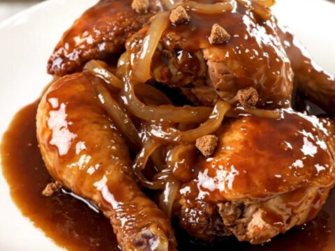 A close-up of slow-cooked chicken thighs covered in a rich, dark glossy sauce served on a white plate.