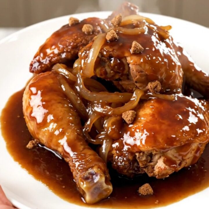A close-up of slow-cooked chicken thighs covered in a rich, dark glossy sauce served on a white plate.