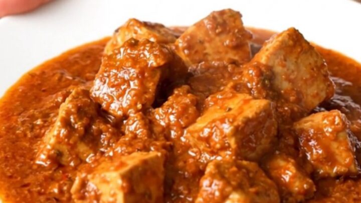 A top-down view of a slow cooker filled with raw pork, onions, and curry sauce, ready for cooking.
