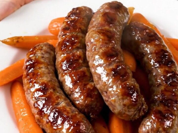 A rustic stew of pork sausages and sliced carrots in a savory white wine sauce served on a white plate.
