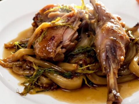 A close-up of tender, slow-cooked rabbit pieces with caramelized fennel served on a white plate.