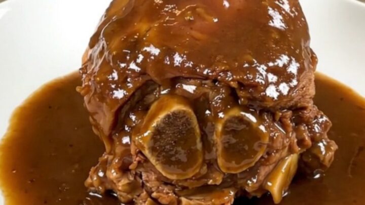 A tender slow-cooked amber beer veal shank served on a white plate with a glossy sauce.