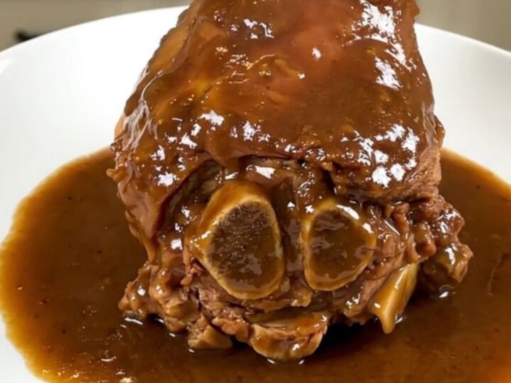 A tender slow-cooked amber beer veal shank served on a white plate with a glossy sauce.
