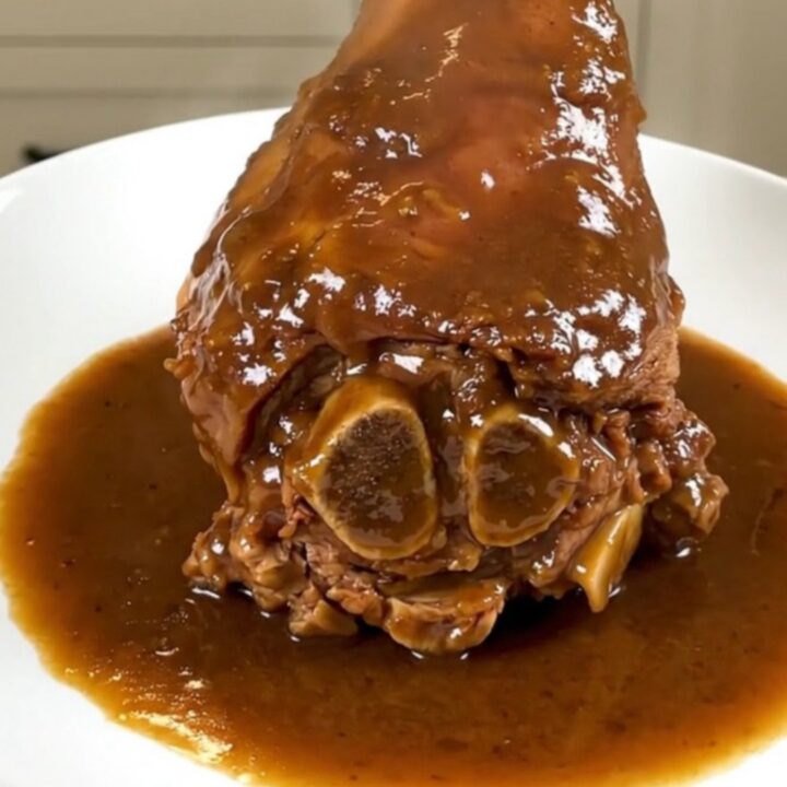 A tender slow-cooked amber beer veal shank served on a white plate with a glossy sauce.