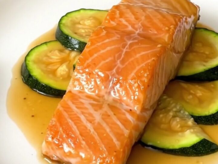 A close-up view of cooked salmon fillets and zucchini in a black slow cooker, drizzled with a glossy honey mustard glaze.