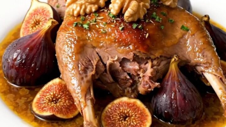 A slow cooker filled with braised duck legs, dried figs, and onions in a rich, spiced sauce on a quartz countertop.