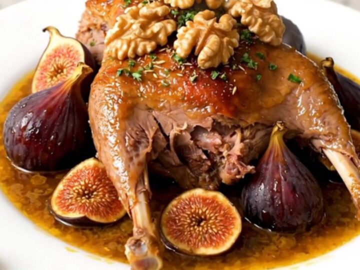 A slow cooker filled with braised duck legs, dried figs, and onions in a rich, spiced sauce on a quartz countertop.