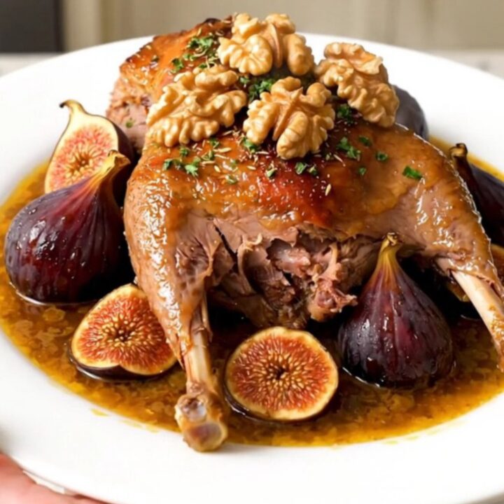 A slow cooker filled with braised duck legs, dried figs, and onions in a rich, spiced sauce on a quartz countertop.