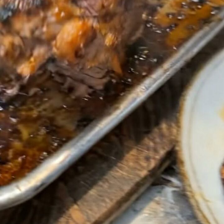 A golden-brown roasted chicken in a metal pan with a glossy honey-garlic glaze and bubbling pan juices.