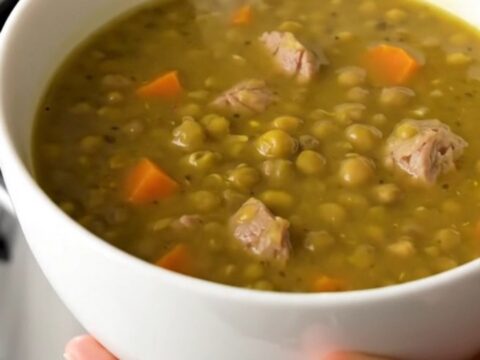 A steaming bowl of split pea and smoked sausage soup with visible sausage rounds and diced carrots.