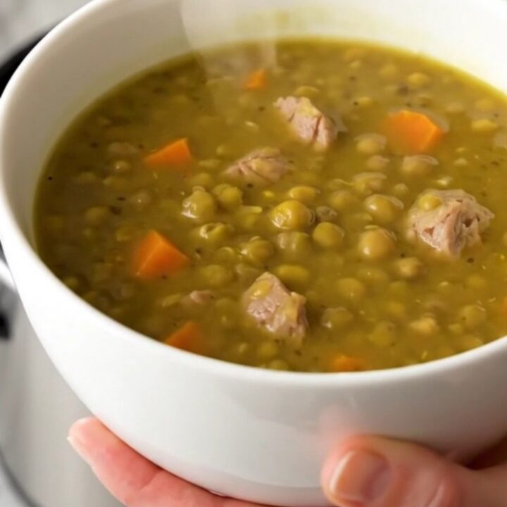 A steaming bowl of split pea and smoked sausage soup with visible sausage rounds and diced carrots.