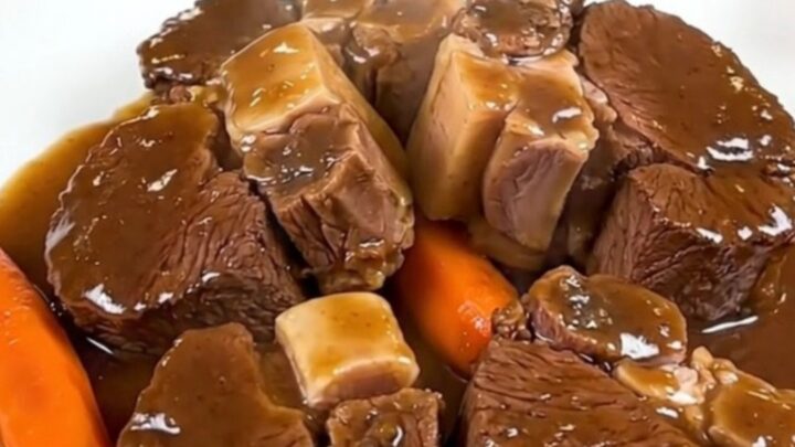 A close-up of tender, glossy beef cheeks in a rich dark sauce served with carrots on a white plate.