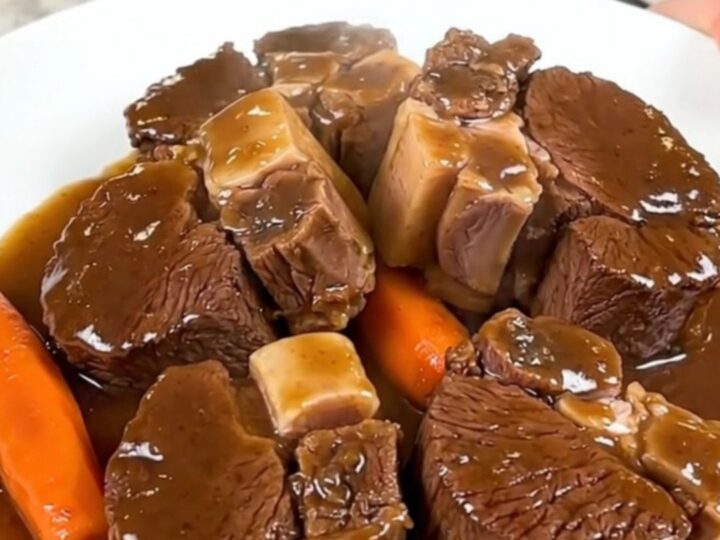 A close-up of tender, glossy beef cheeks in a rich dark sauce served with carrots on a white plate.