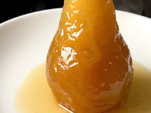 A close-up of a perfectly poached, glistening pear served on a clean white plate.