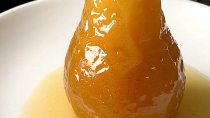 A close-up of a perfectly poached, glistening pear served on a clean white plate.