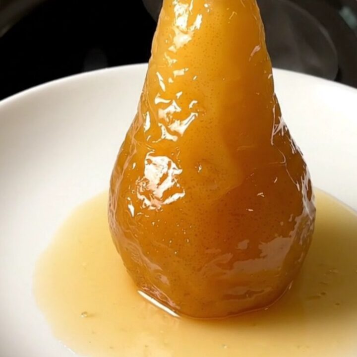 A close-up of a perfectly poached, glistening pear served on a clean white plate.