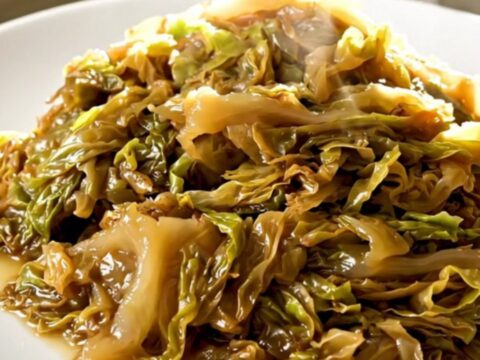 A top-down view of a black slow cooker filled with layers of sliced onions and shredded green cabbage.
