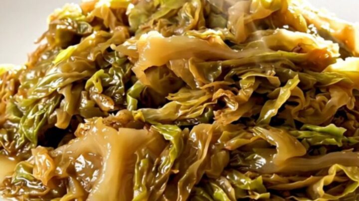 A top-down view of a black slow cooker filled with layers of sliced onions and shredded green cabbage.