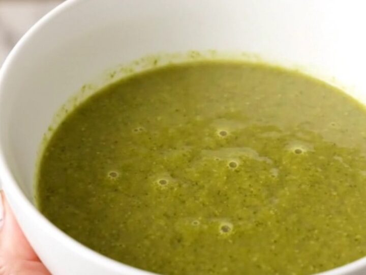 A white bowl filled with creamy green broccoli soup, garnished with a crumble of Roquefort cheese.