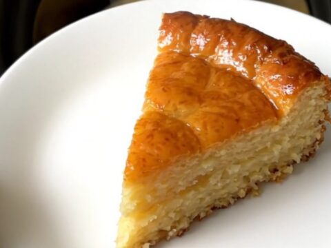 A golden-brown slice of warm apple far served on a white plate, showing a soft custard texture and apple slices.