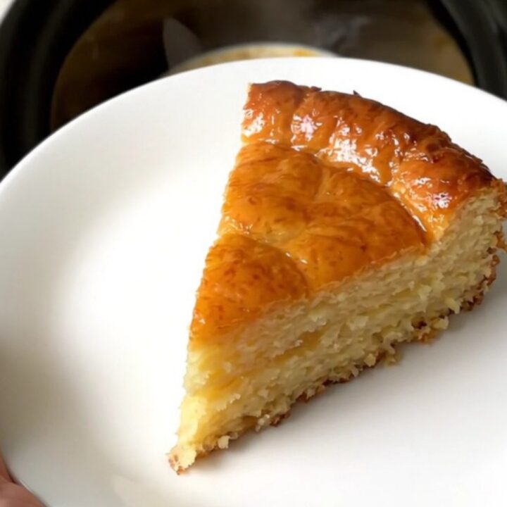 A golden-brown slice of warm apple far served on a white plate, showing a soft custard texture and apple slices.