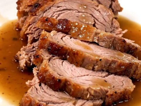 A succulent, slow-cooked pork roast served on a white plate with glossy pan juices.