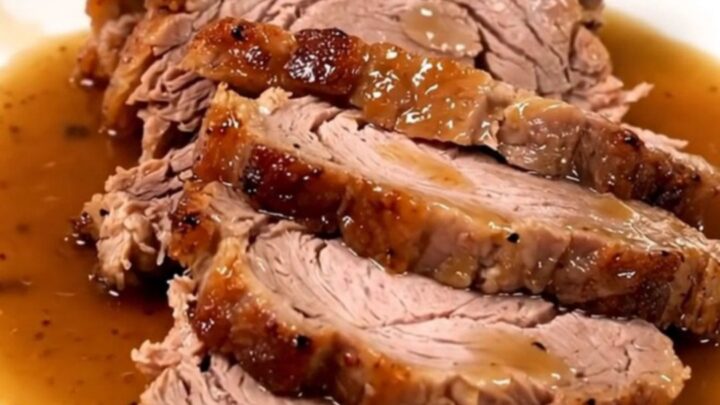 A succulent, slow-cooked pork roast served on a white plate with glossy pan juices.