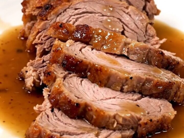 A succulent, slow-cooked pork roast served on a white plate with glossy pan juices.